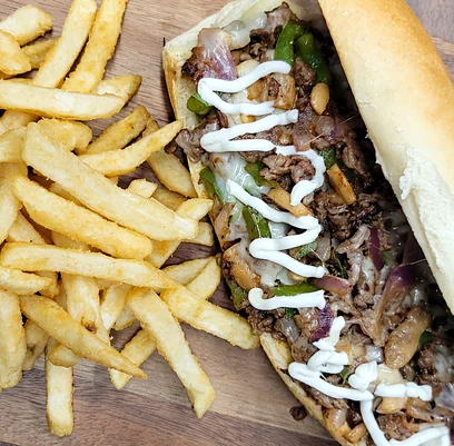 Sub roll filled with grilled shaved meat, peppers and white sauce, beside fries
