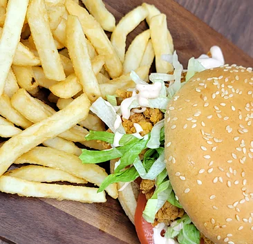 Crispy chicken burger with lettuce beside fries on a wooden board