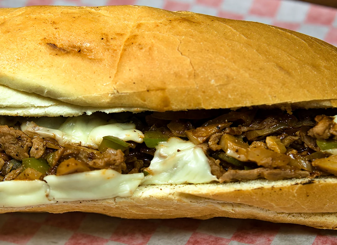 Philly cheese steak on a long roll with grilled meat, peppers, mushrooms and melted cheese