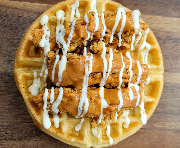 Waffle topped with chicken tenders and a drizzle of sauce